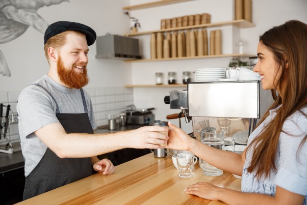 coffee business concept young beared handsome barista talking and giving take away hot coffee for beautiful caucasian customer in modern coffee shop 1258 613
